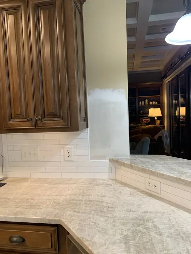 Light stone countertop meeting a white subway tile backsplash beside dark stained cabinets
