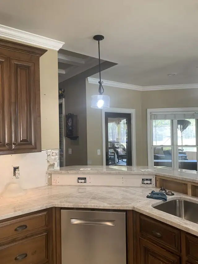 Angled stone countertop run with a raised section and outlet, during backsplash work